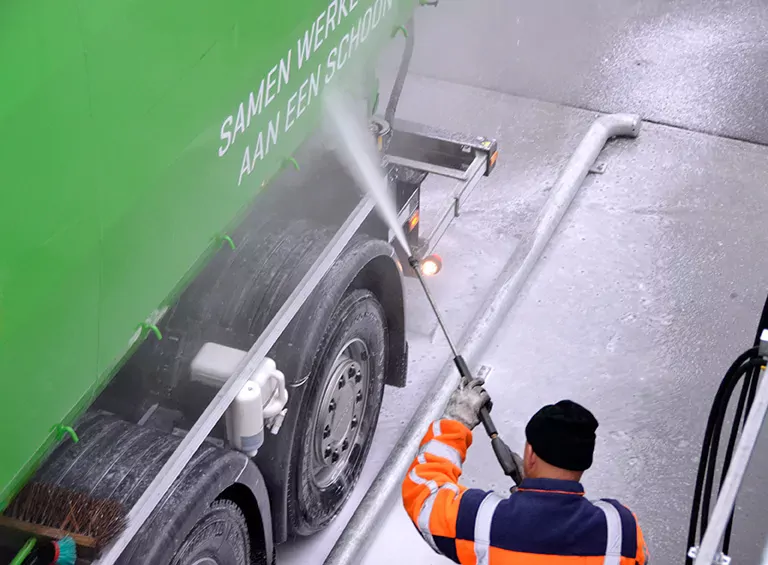 Ingeschuimde zijde van vrachtauto wordt schoongespoten met hogedruk. Schuim op wasvloer stroomt naar afvalwateropvang.