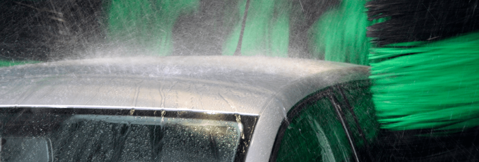 De bovenkant van een auto waar het water als hevige regen op neerkomt omdat het wordt gewassen door de hogedruksproeiers van een roll over carwash