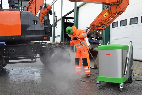 At the front a DiBO hot water high pressure washer IBH-L. In the back you see a person in protective clothes who cleans a truck