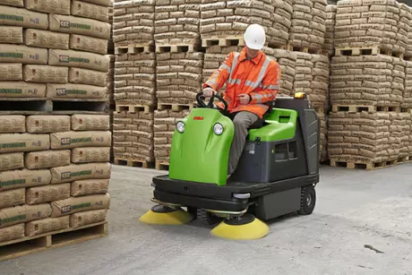 Sweeping a corridor in a warehouse with a DiBO sweeper. In the background, brown bags are stored on pallets