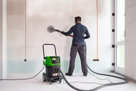 Man sanding wall with sander connected to safety vacuum cleaner DiBO P35 WDM for dust-free work