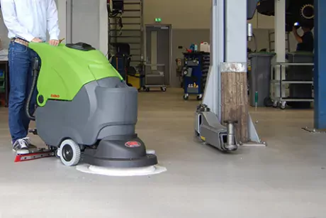 Person with a DiBO walk behind scrubber-dryer cleans the floor of a garage workshop